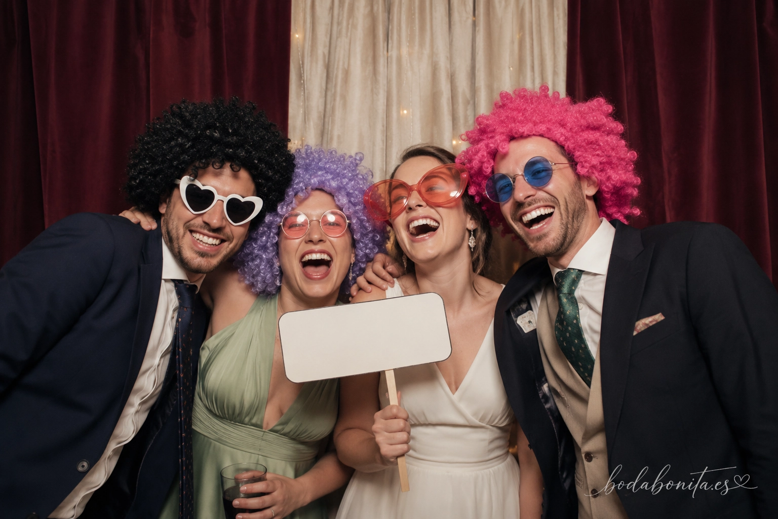 grupo de invitados riendo y posando con atrezo divertido en el fotomatón de una boda